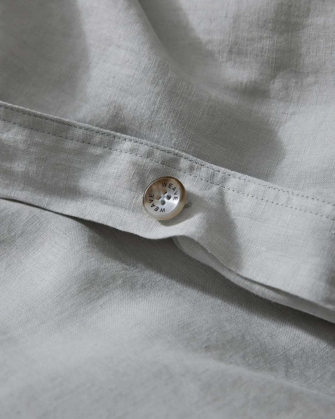 Ravello Quilt Cover Silver detail showing branded Weave Home button closure on French Flax linen by Weave Home