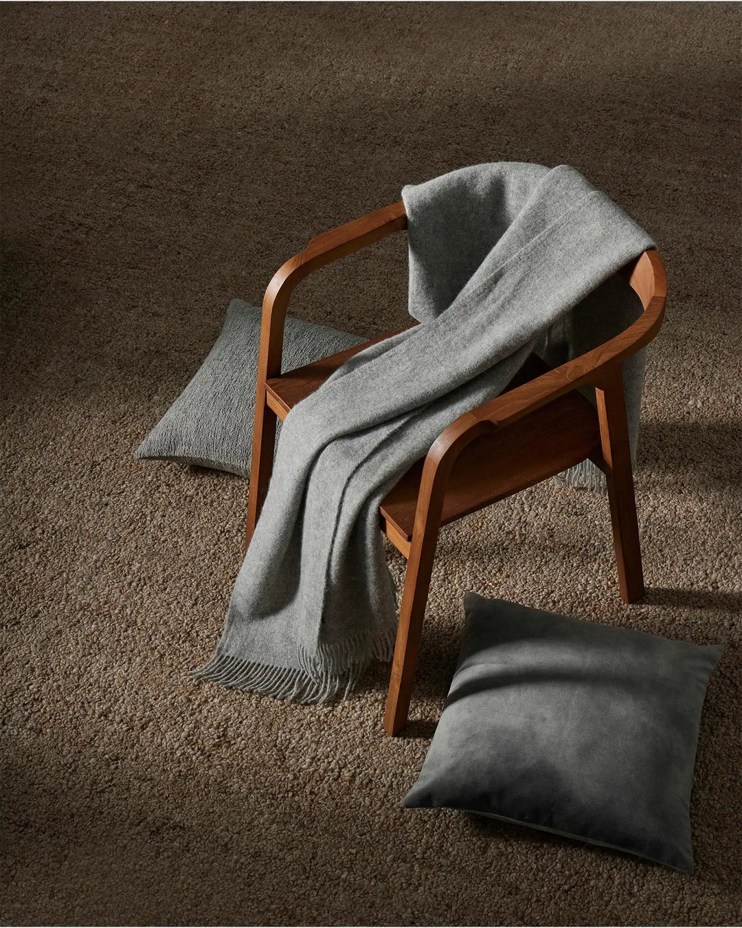 Mid-century modern chair in warm timber with light grey throw and cushion on taupe wool-blend rug, neutral minimalist styling