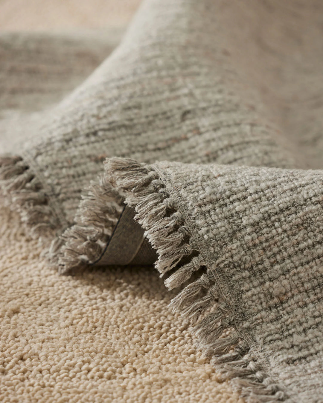 Close-up of neutral textured rugs with fringed edges, showcasing layered cream and beige tones and woven wool-blend fabrics in contemporary home styling