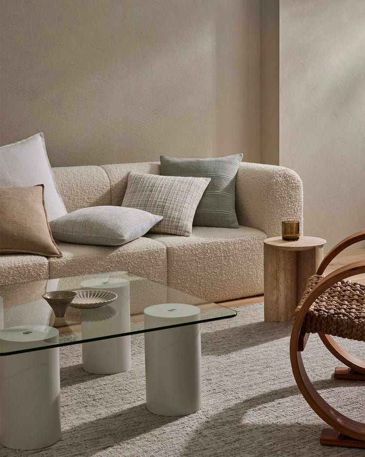 Neutral minimalist living room with cream boucle sofa layered with linen cushions, natural wood accents, and soft beige area rug for contemporary Scandinavian interiors