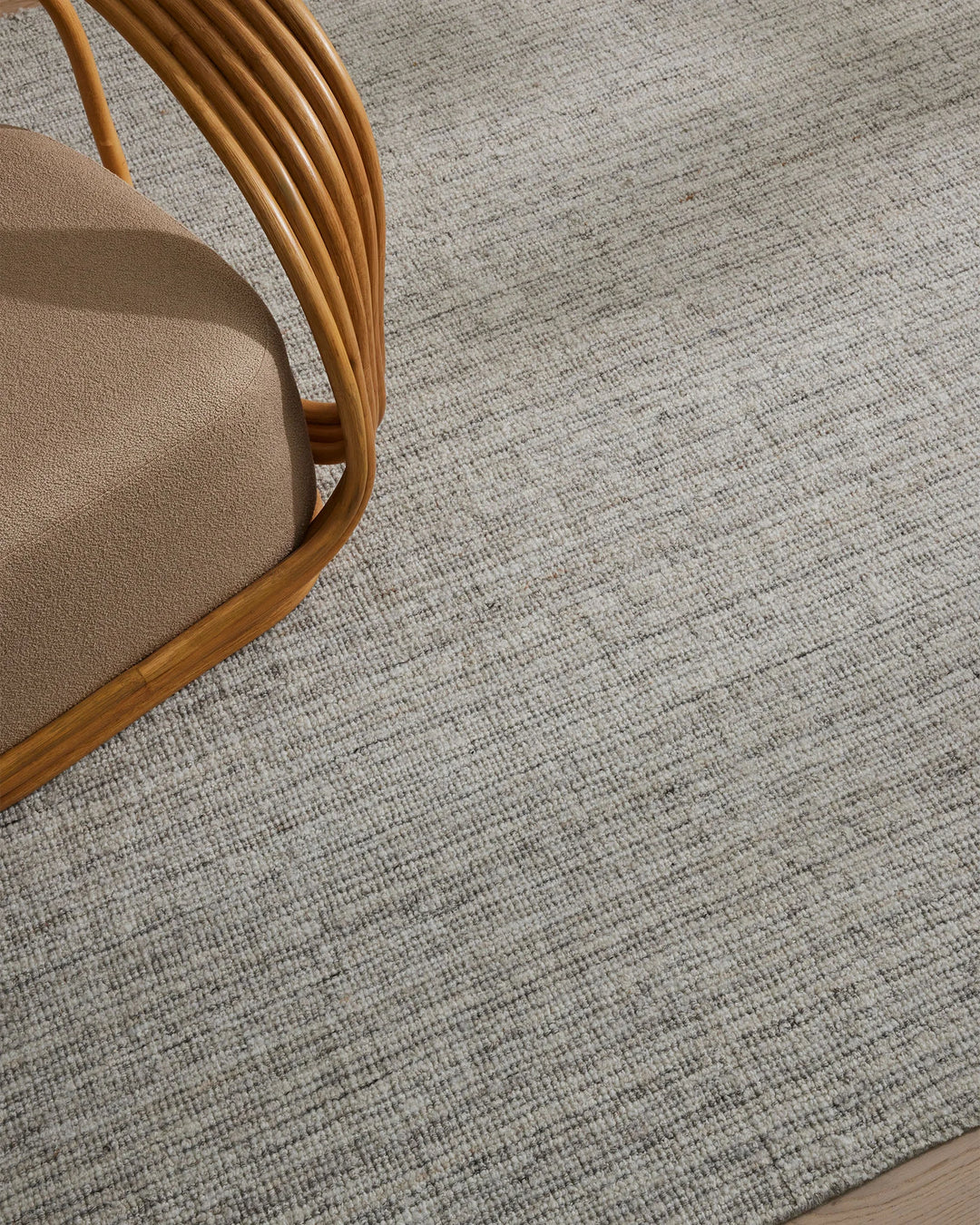 Neutral wool-blend rug with woven texture beneath mid-century wooden chair upholstered in warm taupe, minimalist Scandinavian interior styling