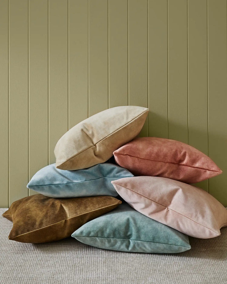 Stacked Ava cushions in earthy palette of seaglass, blush, burnish, nougat and powder against sage green panelled wall and neutral linen floor