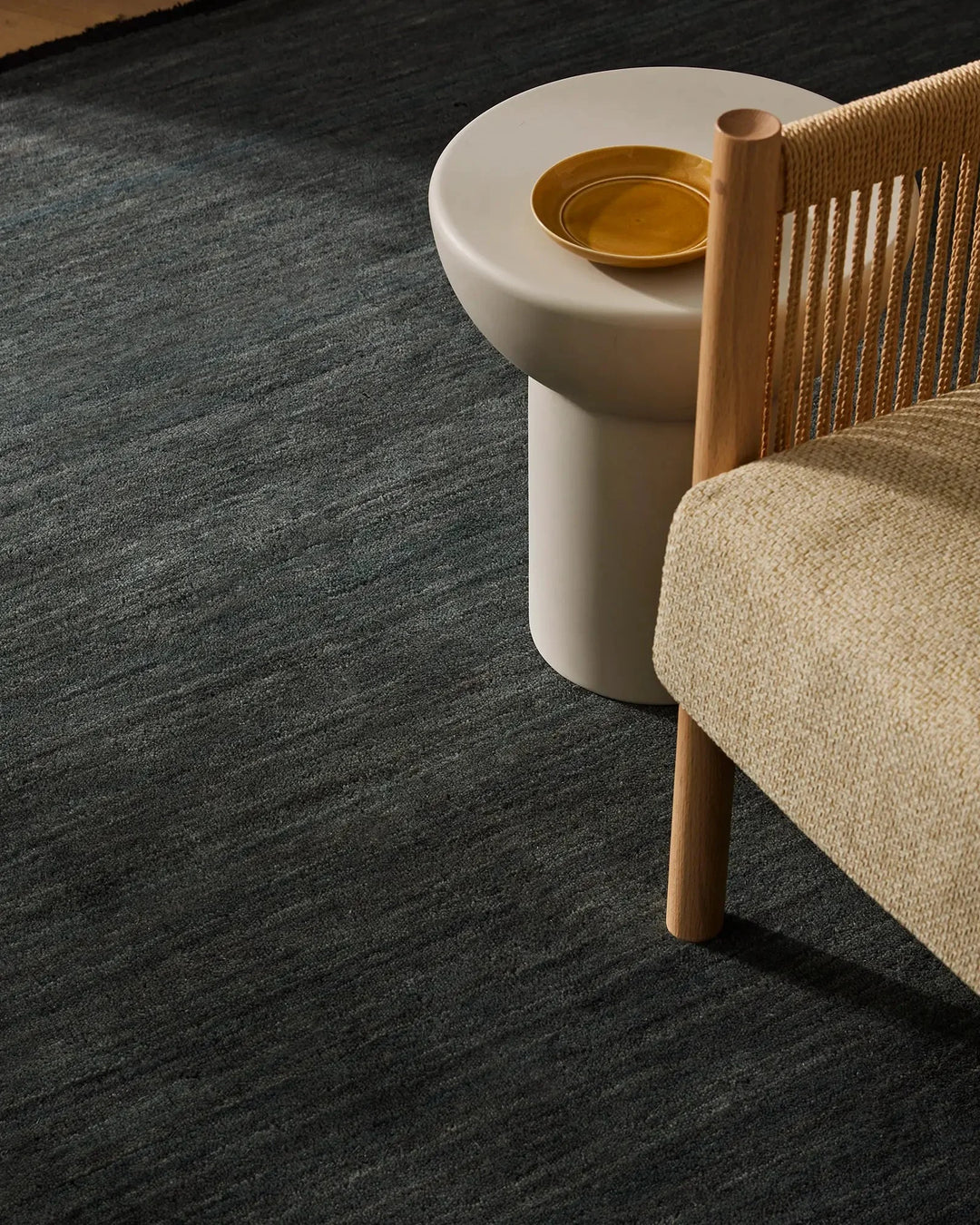 Charcoal melange high-traffic rug anchors a minimalist living space with natural wood chair, linen upholstery, and warm brass accents
