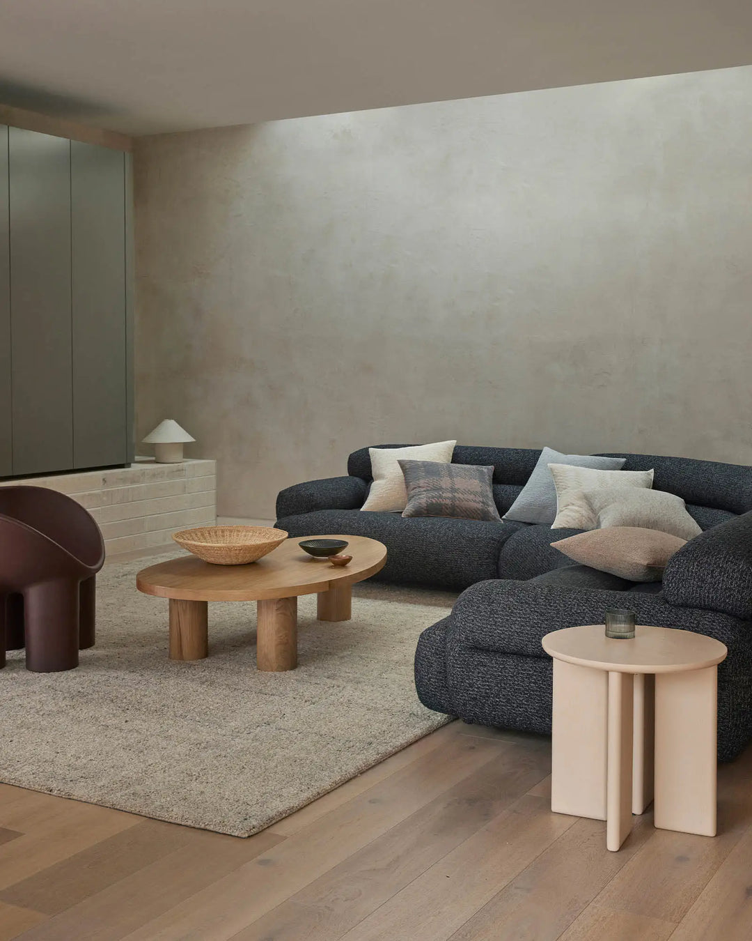 Minimalist living room with charcoal curved sofa dressed in Laurent cushions in mist and mushroom tones, natural wood coffee table, beige linen rug, and soft neutral palette with warm wood floors
