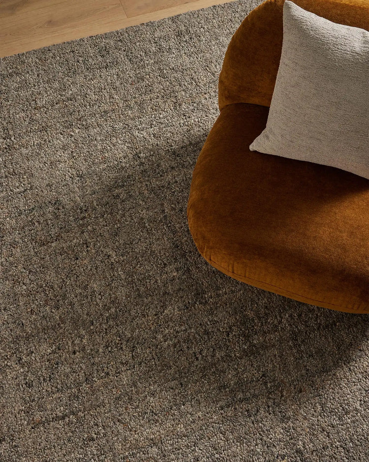 Warm minimalist living room with ochre velvet chair, natural linen cushion, and textured neutral wool-blend area rug on wooden flooring