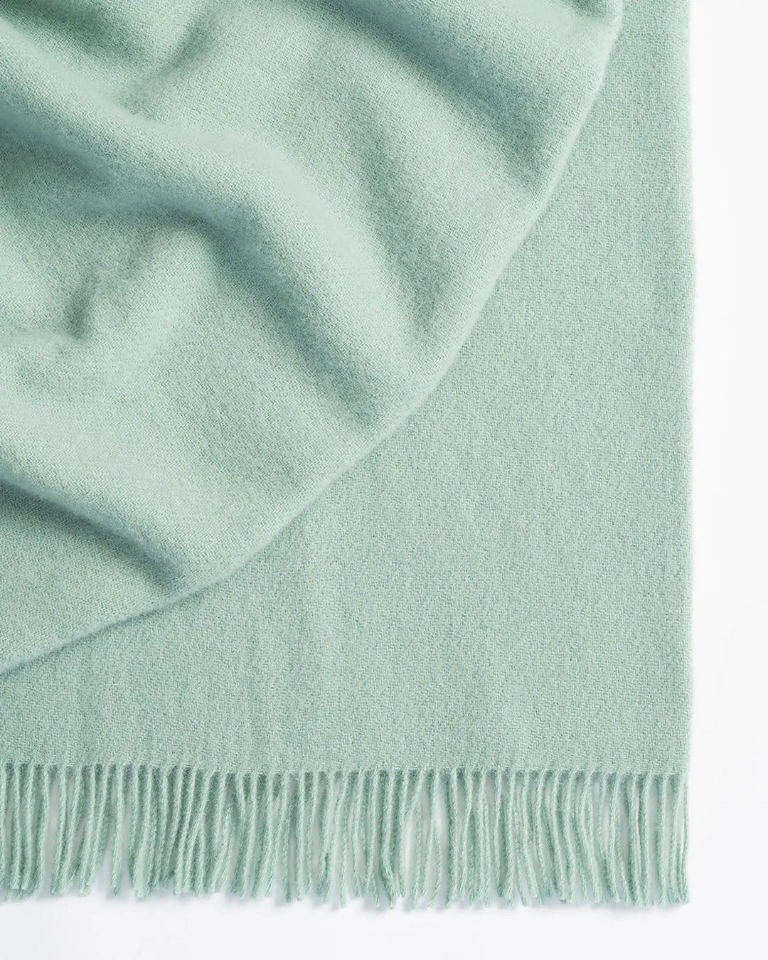 Nevis Mineral throw in pale blue lambswool, close-up showing soft texture and tassel fringe border by Weave Home