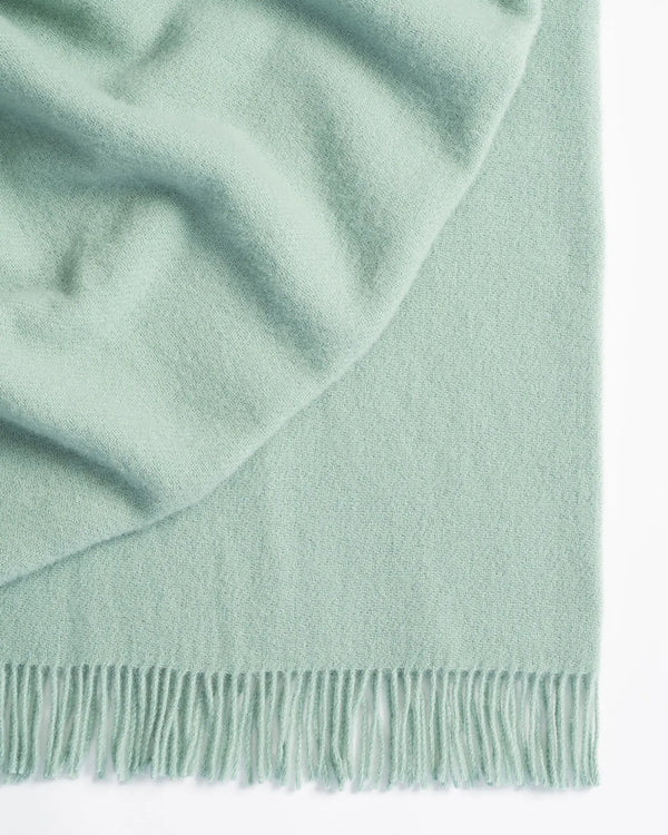Nevis Mineral throw in pale blue lambswool, close-up showing soft texture and tassel fringe border by Weave Home