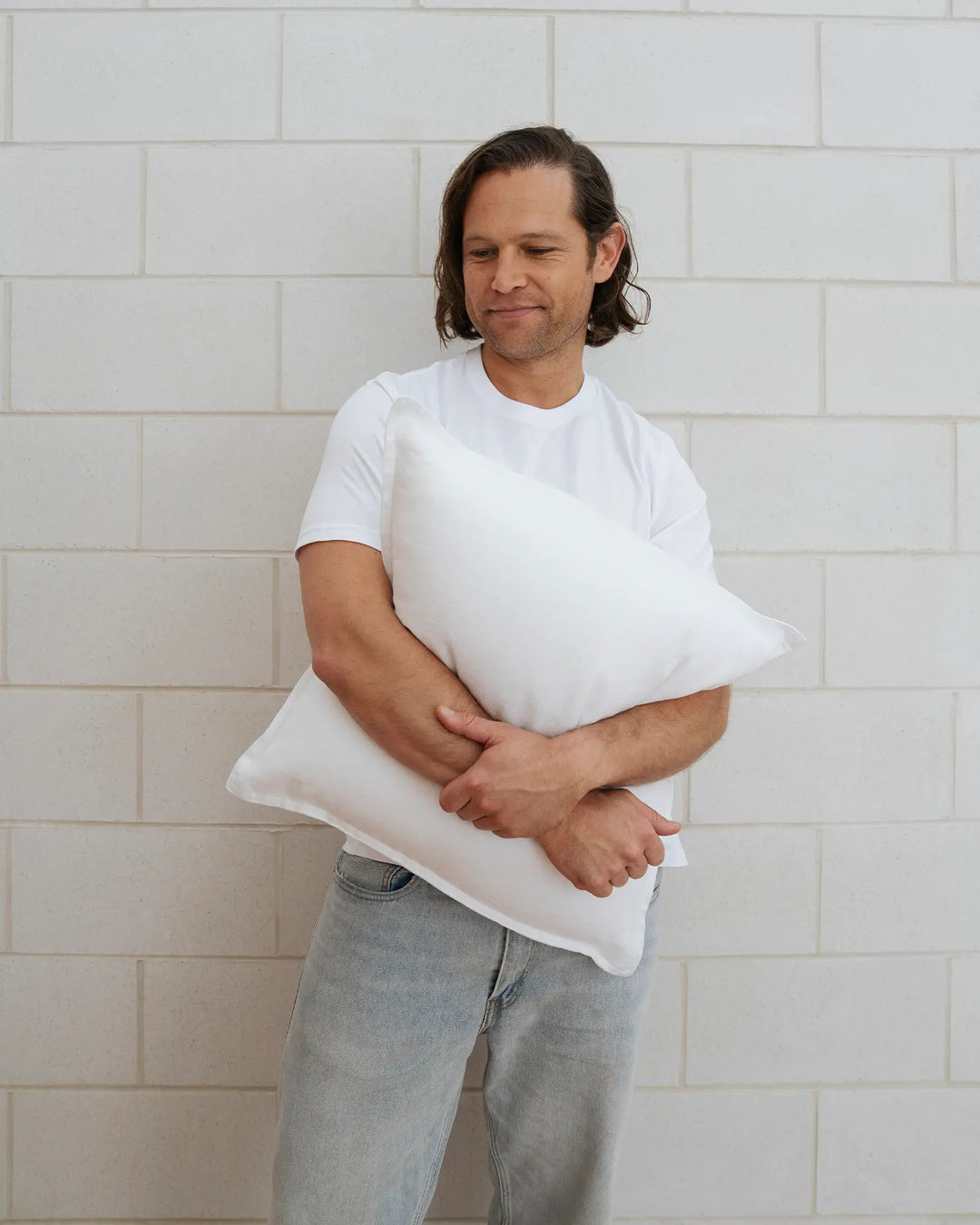 Como Snow cushion in white European linen, 50x50cm, held by model against brick wall, showcasing soft stonewashed texture by Weave Home