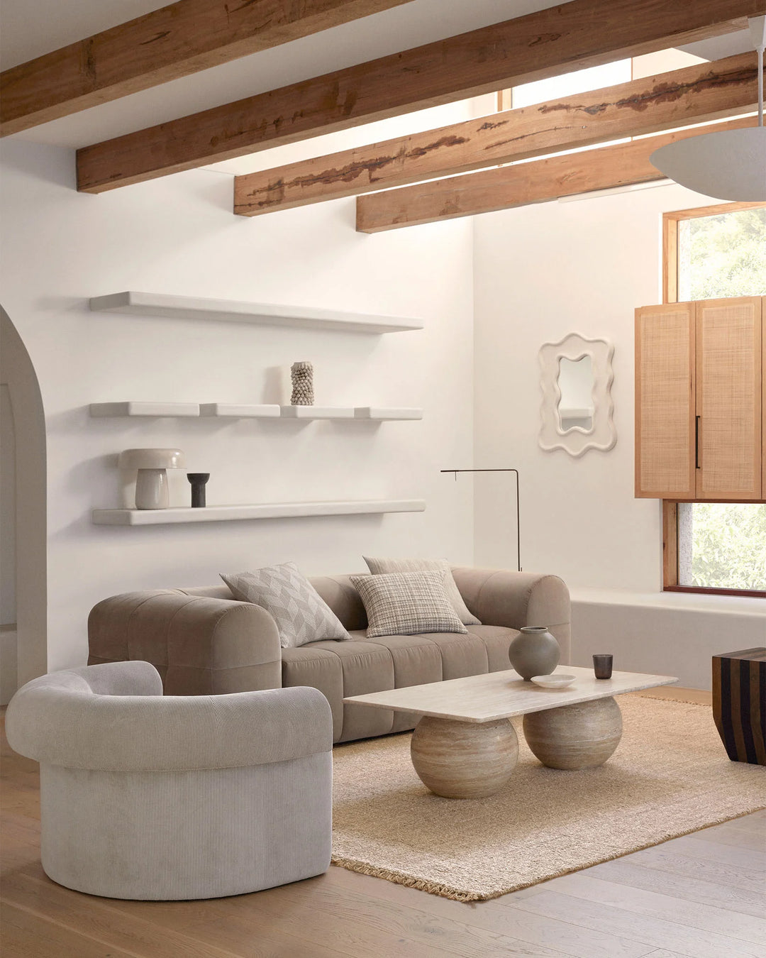 Neutral living room with exposed timber beams, cream and taupe upholstered seating, natural linen cushions, and woven hemp rug layered over light timber flooring