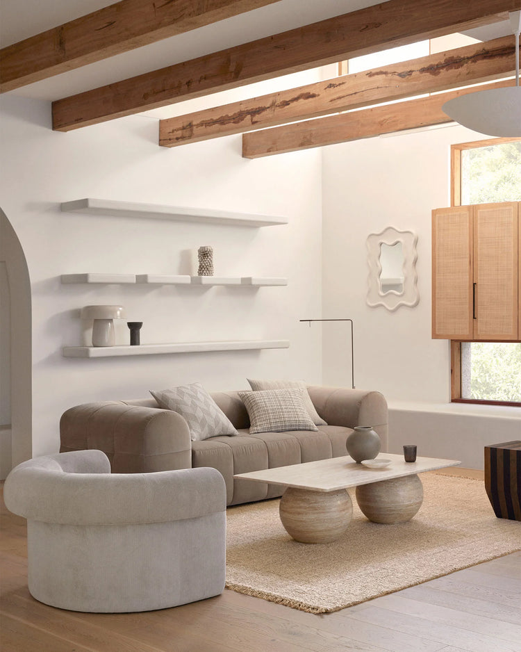 Neutral living room with exposed timber beams, cream and taupe upholstered seating, natural linen cushions, and woven hemp rug layered over light timber flooring