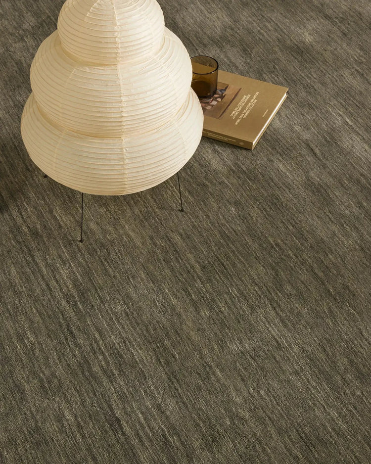 Minimalist interior with charcoal textured rug, cream pleated pendant lamp, and warm neutrals creating a calm, contemporary living space with natural light and layered tones