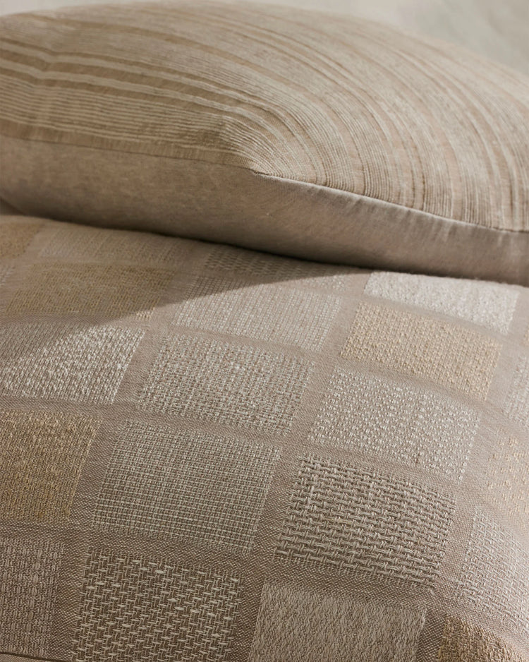 Close-up of neutral linen-cotton cushions layered together, showcasing textured weaves and tonal patchwork patterns in warm beige and cream tones