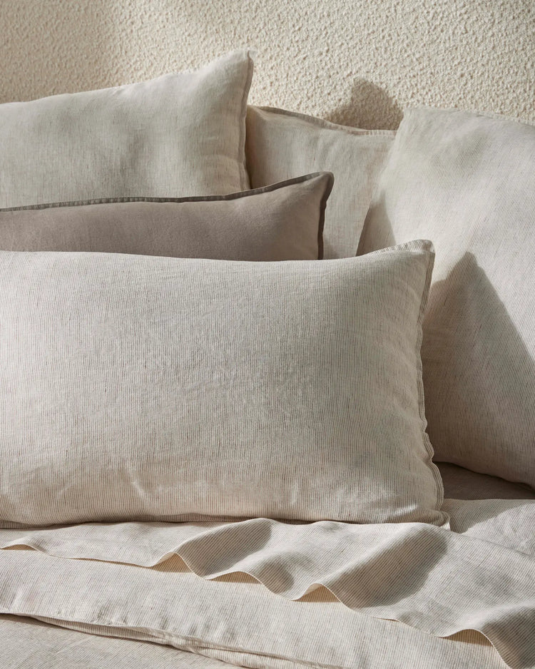 Neutral bedding styled with layered Ravello pillowcases in cream and pebble tones, showcasing ribbed linen textures against a textured cream wall