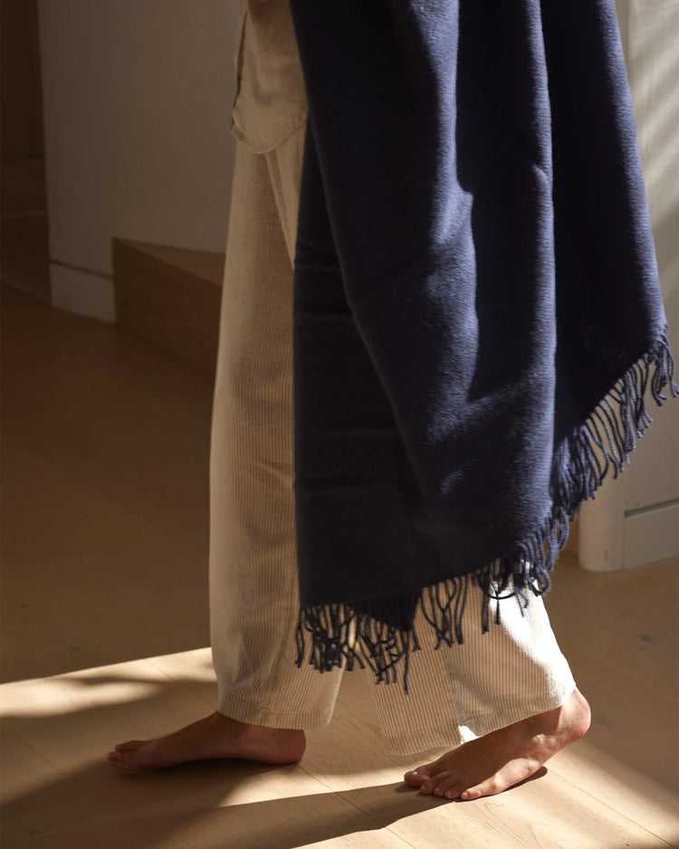 Indigo throw with fringed hem draped over cream knit, styled in warm natural light casting soft shadows on timber floor