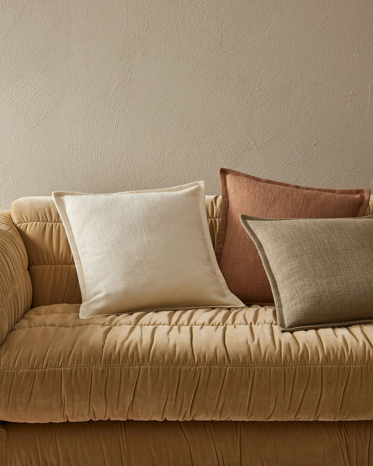 Warm neutral palette with cream, terracotta and beige linen cushions layered on a quilted ochre sofa against textured taupe wall