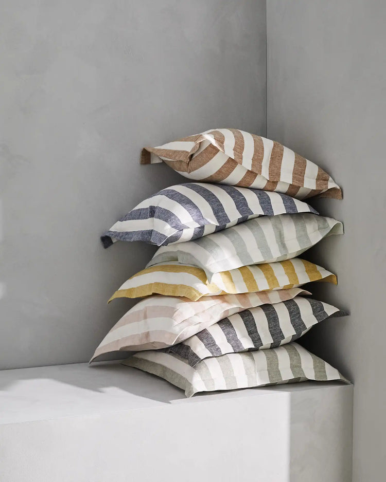 Stacked striped linen blend cushions in neutral and muted tones—clay, ocean, shadow, and sage—against minimal grey wall styling for contemporary home décor