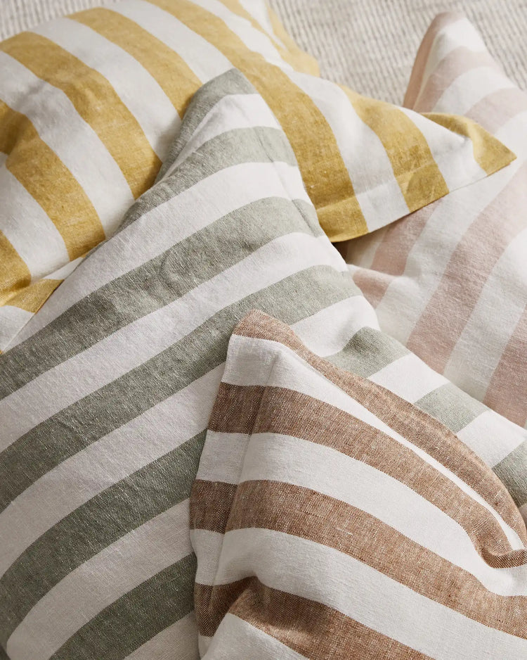 Layered striped linen blend cushions in warm neutral tones—gold, sage, taupe and blush—arranged in soft folds showcasing textured weave and contemporary stripe pattern