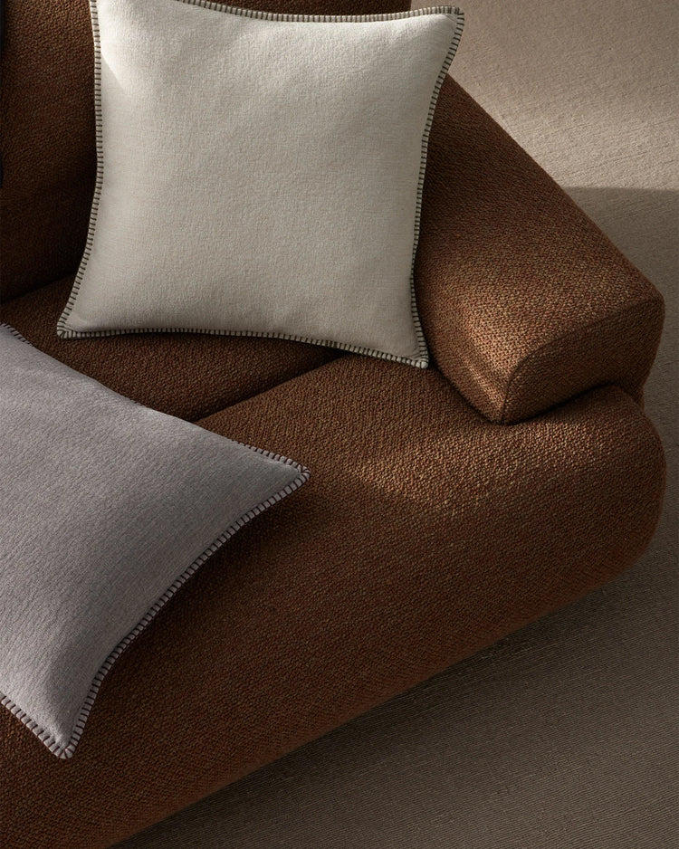 Neutral and chocolate brown textiles layered on a sofa, featuring Alba cushions with contrast blanket stitching in a warm, earthy palette with natural linen textures