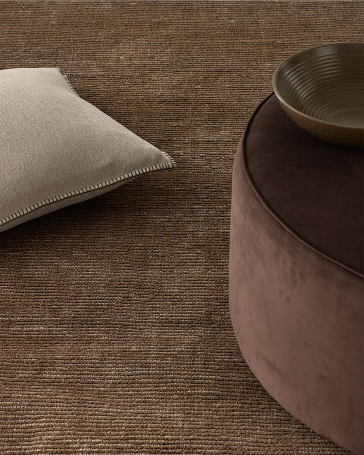 Warm minimalist interior styling neutral palette: Alba Bone cushion on textured Remo Earth wool rug with charcoal ceramic vessel, earthy tones and woven textures