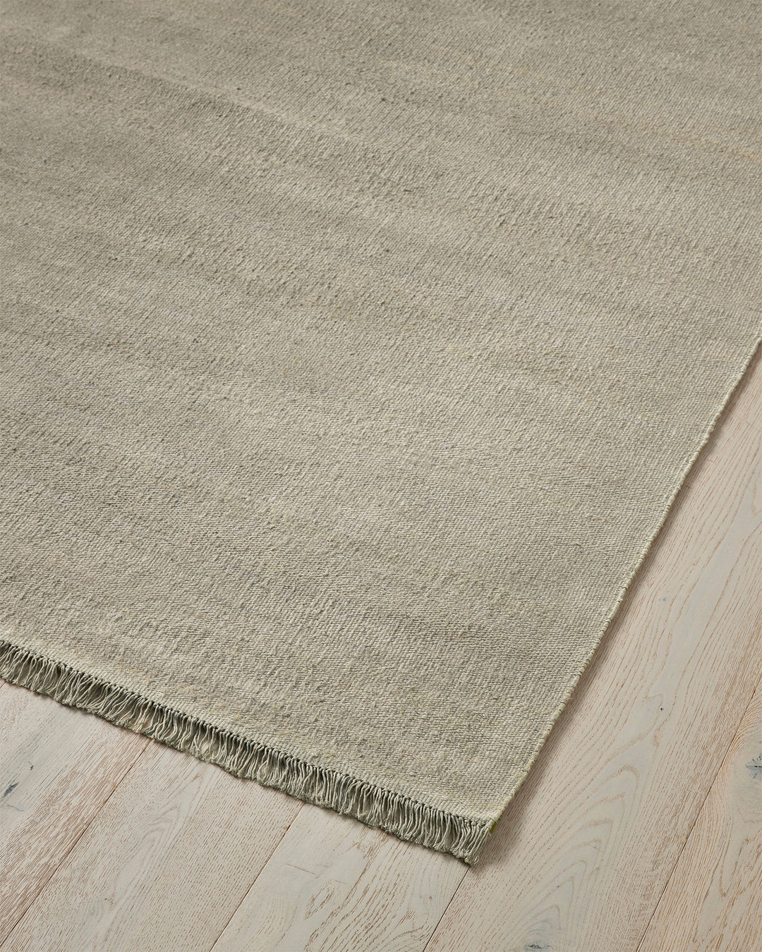 Emilio Oyster linen rug in pale grey, close-up showing flat-weave texture and fringed edge detail by Weave Home