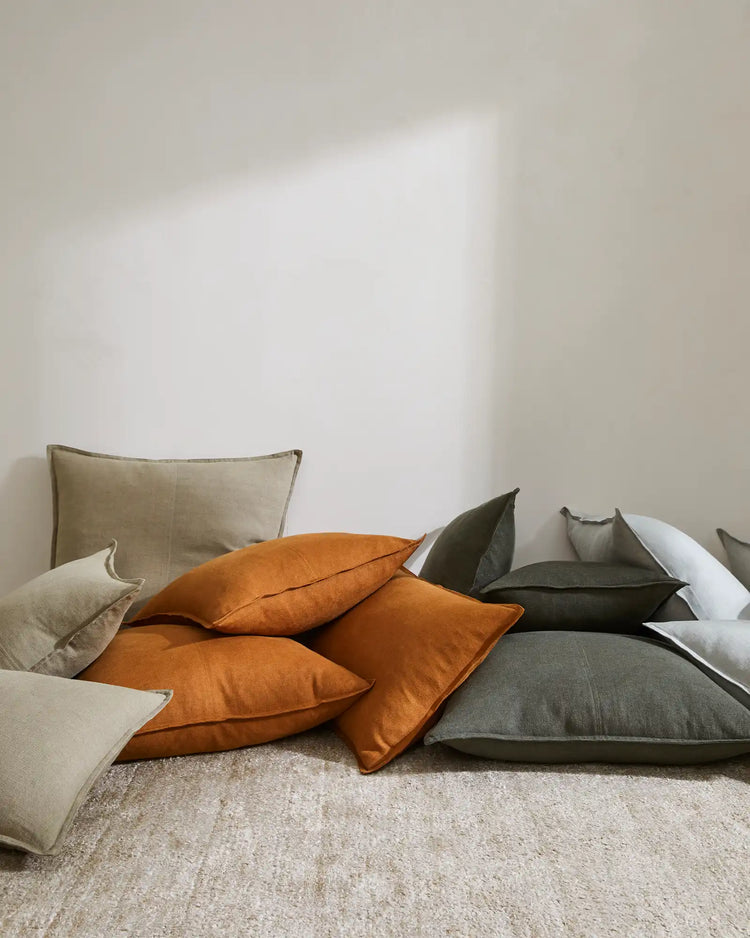 Neutral bedroom styled with Como cushions in spice, caper and khaki linen arranged on a bed with soft natural light, earthy palette and tactile texture