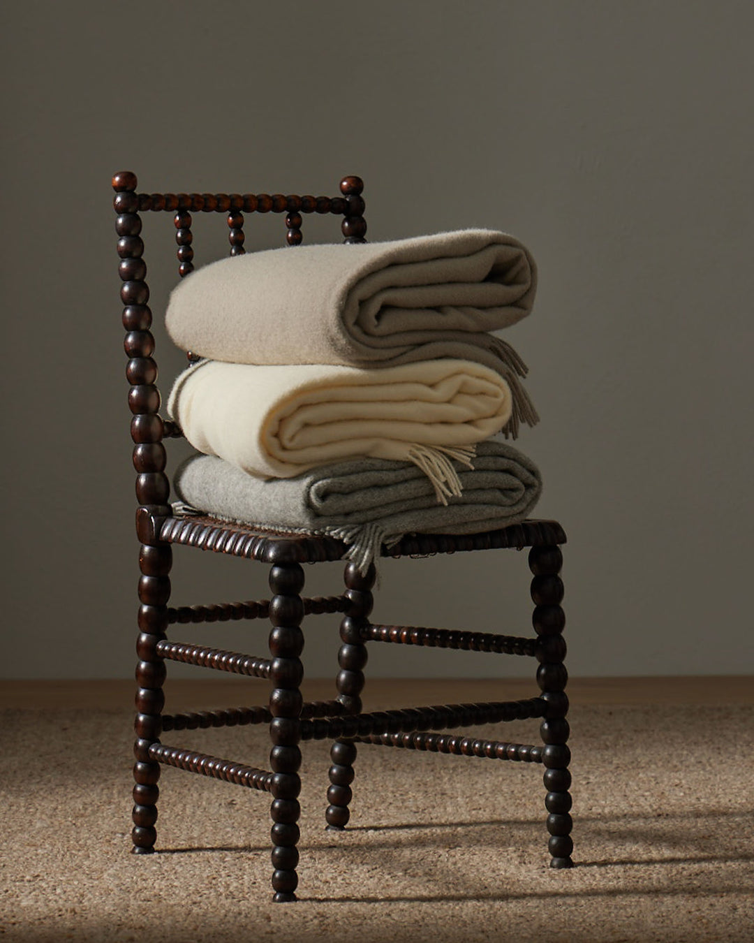 Nevis Limestone lambswool throw in muted grey with tassel border, styled on timber chair by Weave Home