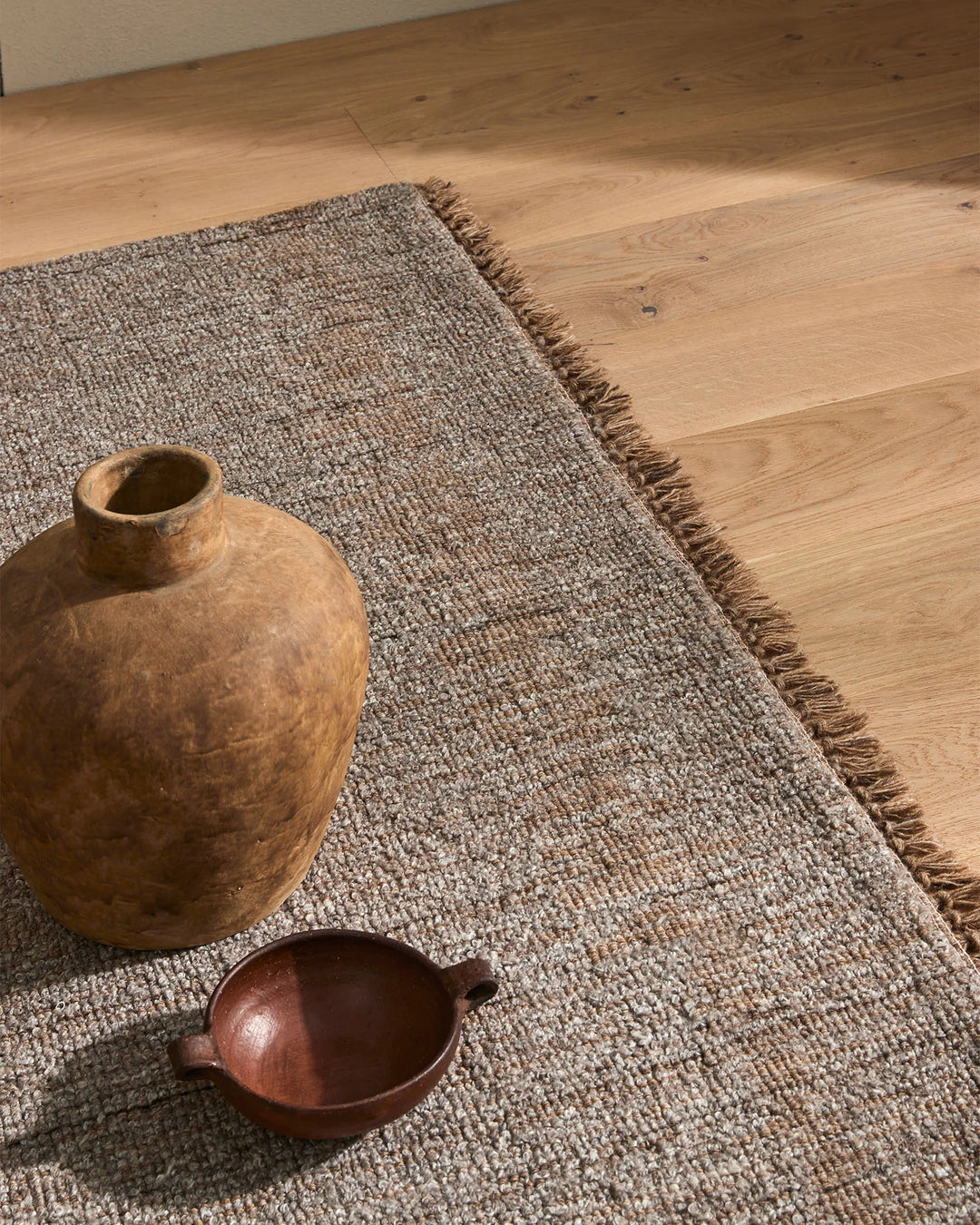 Warm wood flooring styled with taupe wool-blend Puglia rug, natural wooden vessels, and earthy textures creating a minimalist, organic interior aesthetic