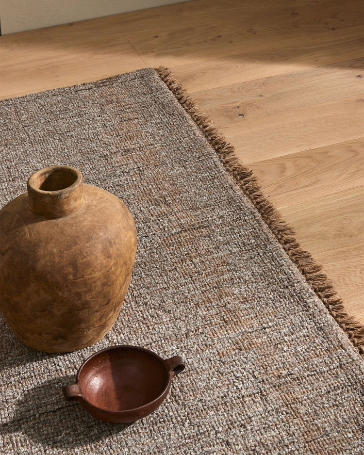 Warm wood flooring styled with taupe wool-blend Puglia rug, natural wooden vessels, and earthy textures creating a minimalist, organic interior aesthetic
