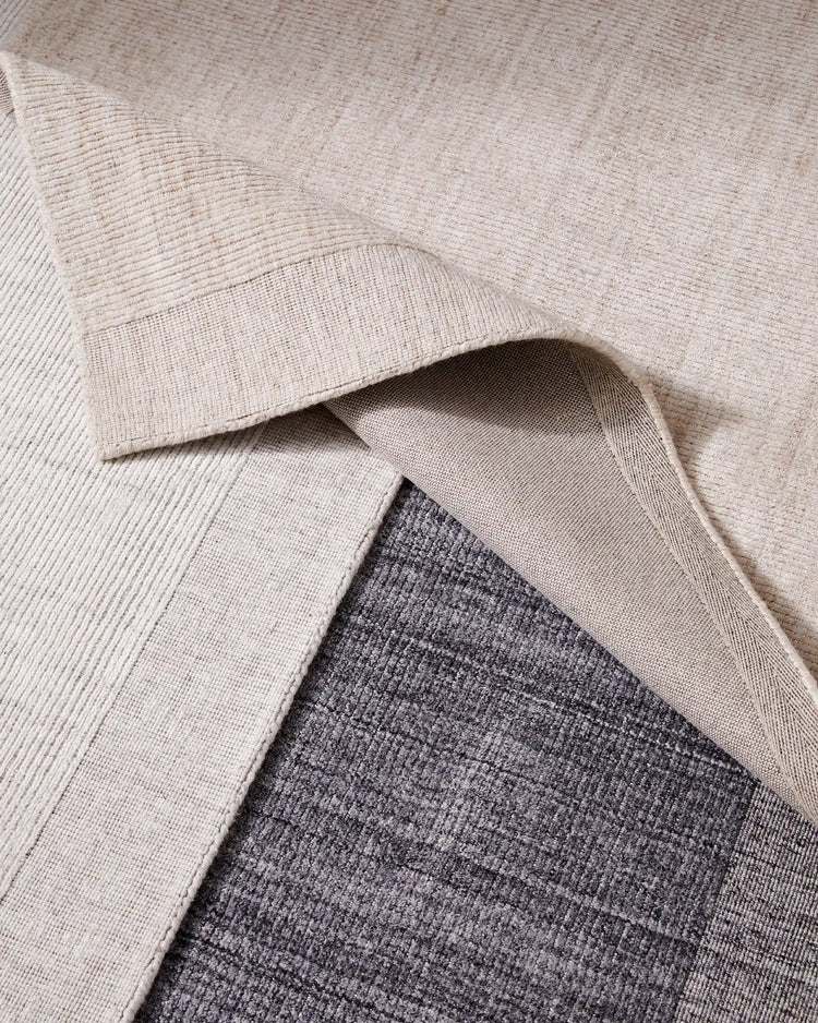Layered neutral rugs in cream and charcoal showcase textured viscose weaves, creating a monochromatic palette with depth and dimension for contemporary interior styling