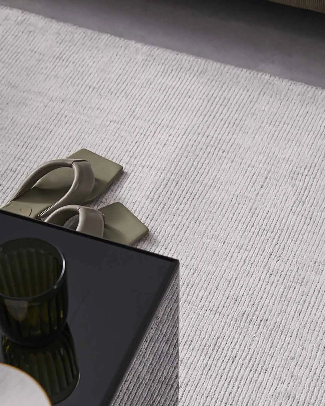 Neutral minimalist bedroom scene with textured viscose Travertine rug in soft grey-white tones, styled with taupe slippers and dark accent table.