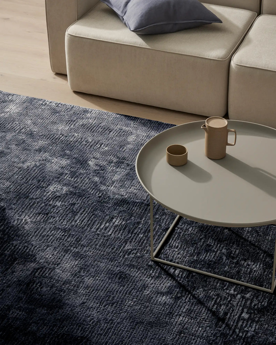 Modern living room with indigo textured rug, cream modular sofa, and navy linen pillow, styled with minimalist round side table and ceramic vessels