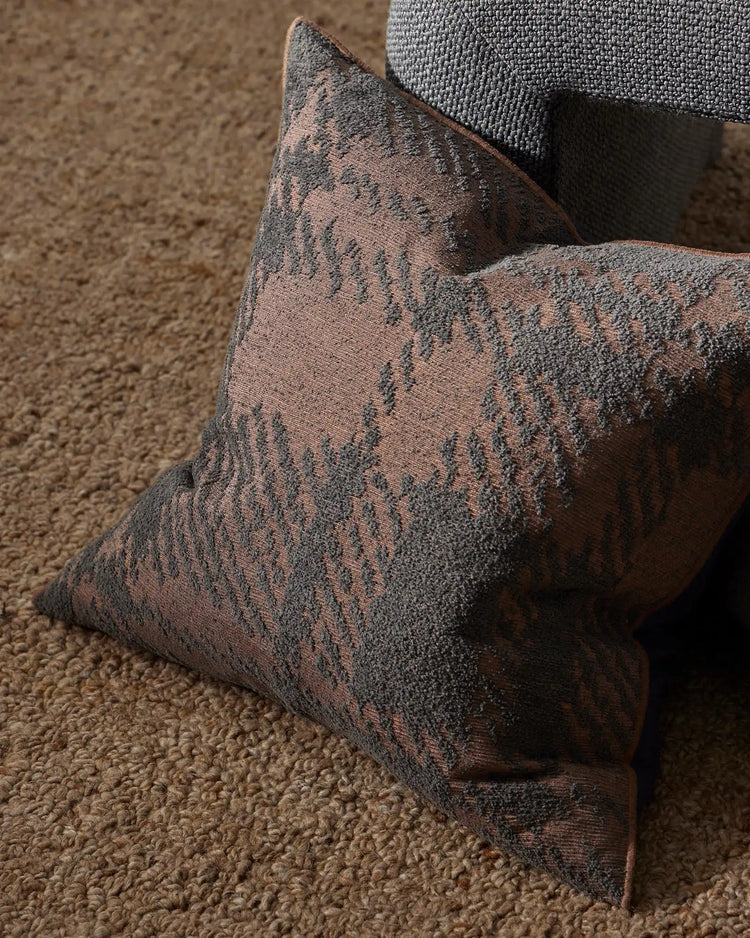 Charcoal and blush geometric cushion layered on neutral textured sofa, styled with woven throw in warm taupe setting