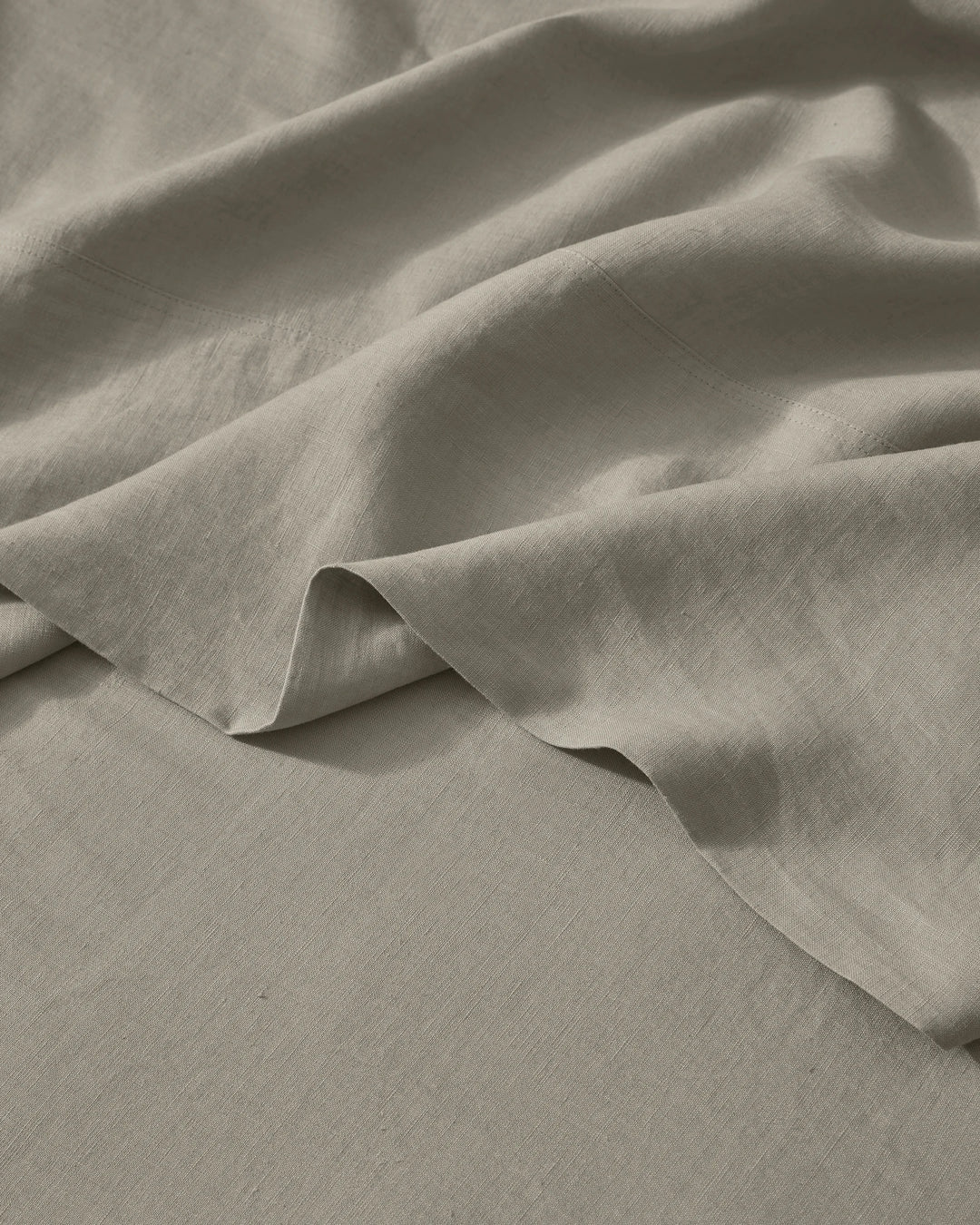 Close-up of soft pebble linen bedding with natural texture and folds, showing lightweight European linen weave in neutral warm tones