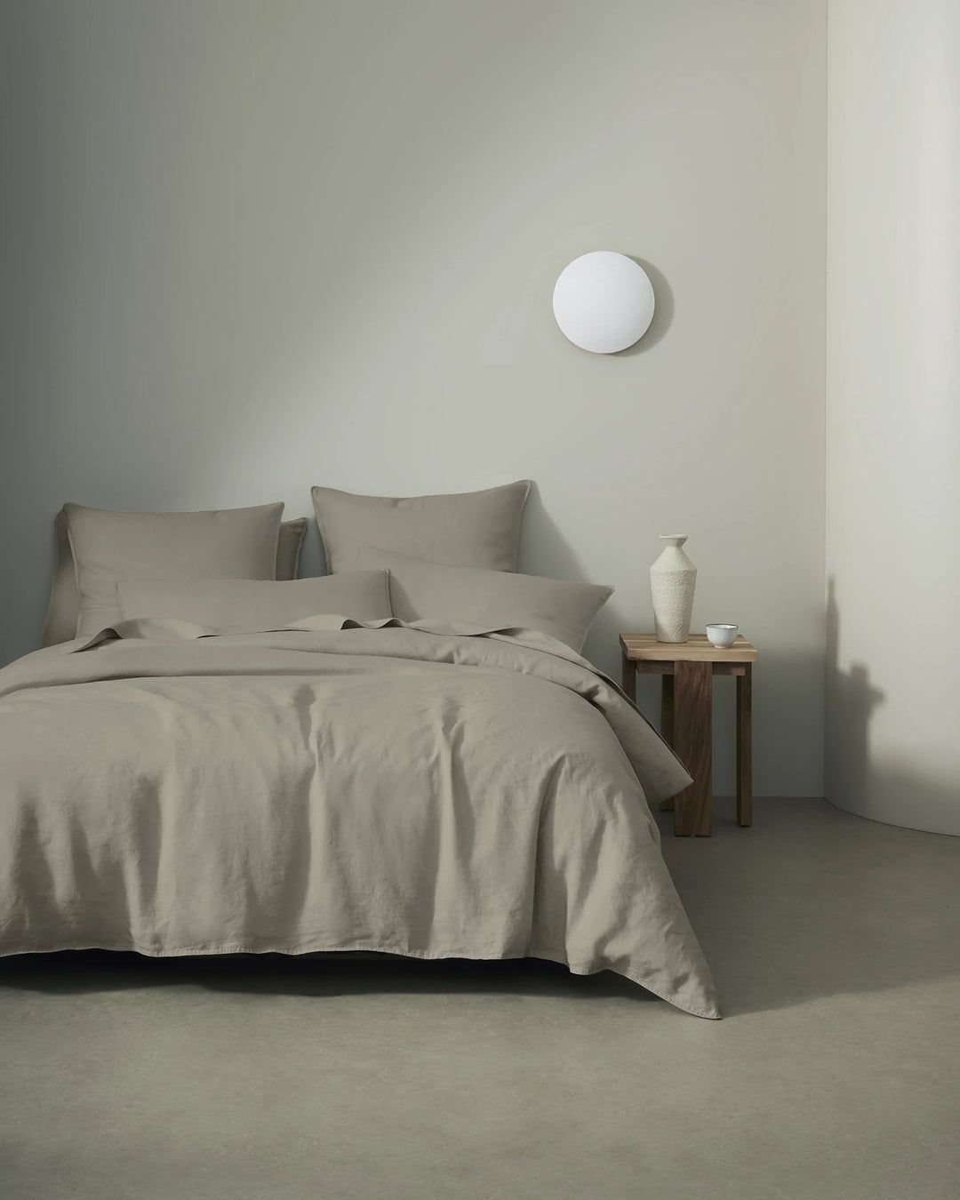 Minimalist bedroom with Ravello linen bedding in pebble grey, featuring soft linen texture and natural draping against neutral walls and warm wood nightstand
