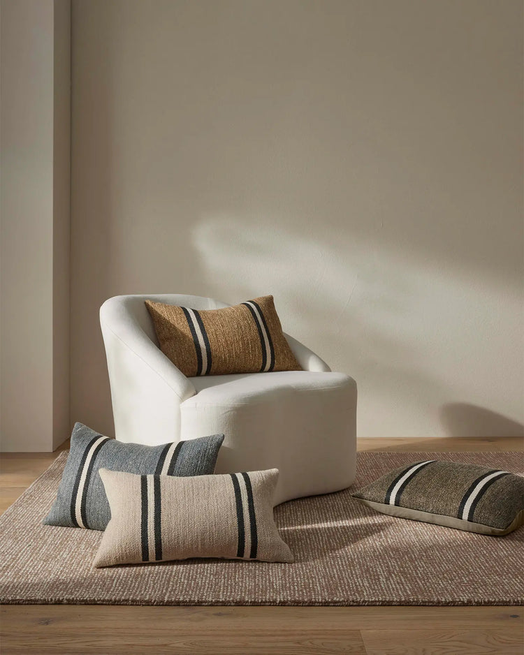 Neutral minimalist interior with cream armchair and Mila cushions in warm earth tones, charcoal stripes, and woven textures on natural fibre rug