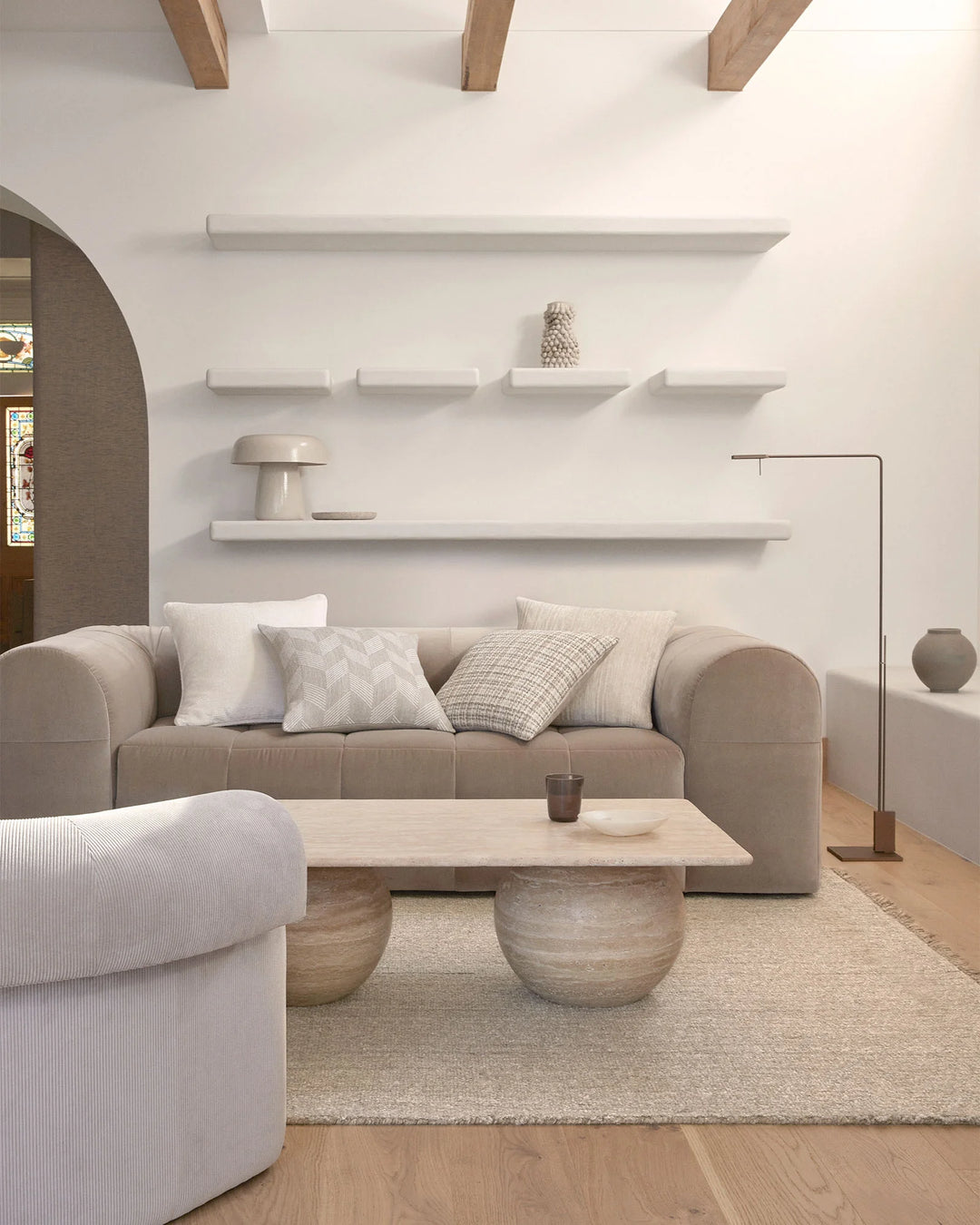 Neutral living room with beige sofa styled with patterned Tempo cushions, natural fibre Puglia rug, wooden coffee table and minimalist white shelving above