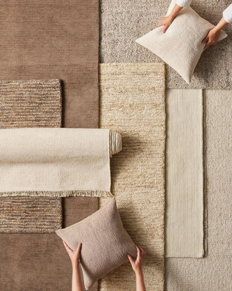 Neutral textile mood board featuring layered woven rugs, throws and cushions in cream, taupe and natural jute tones, displaying texture and material variety from everyday home styling.