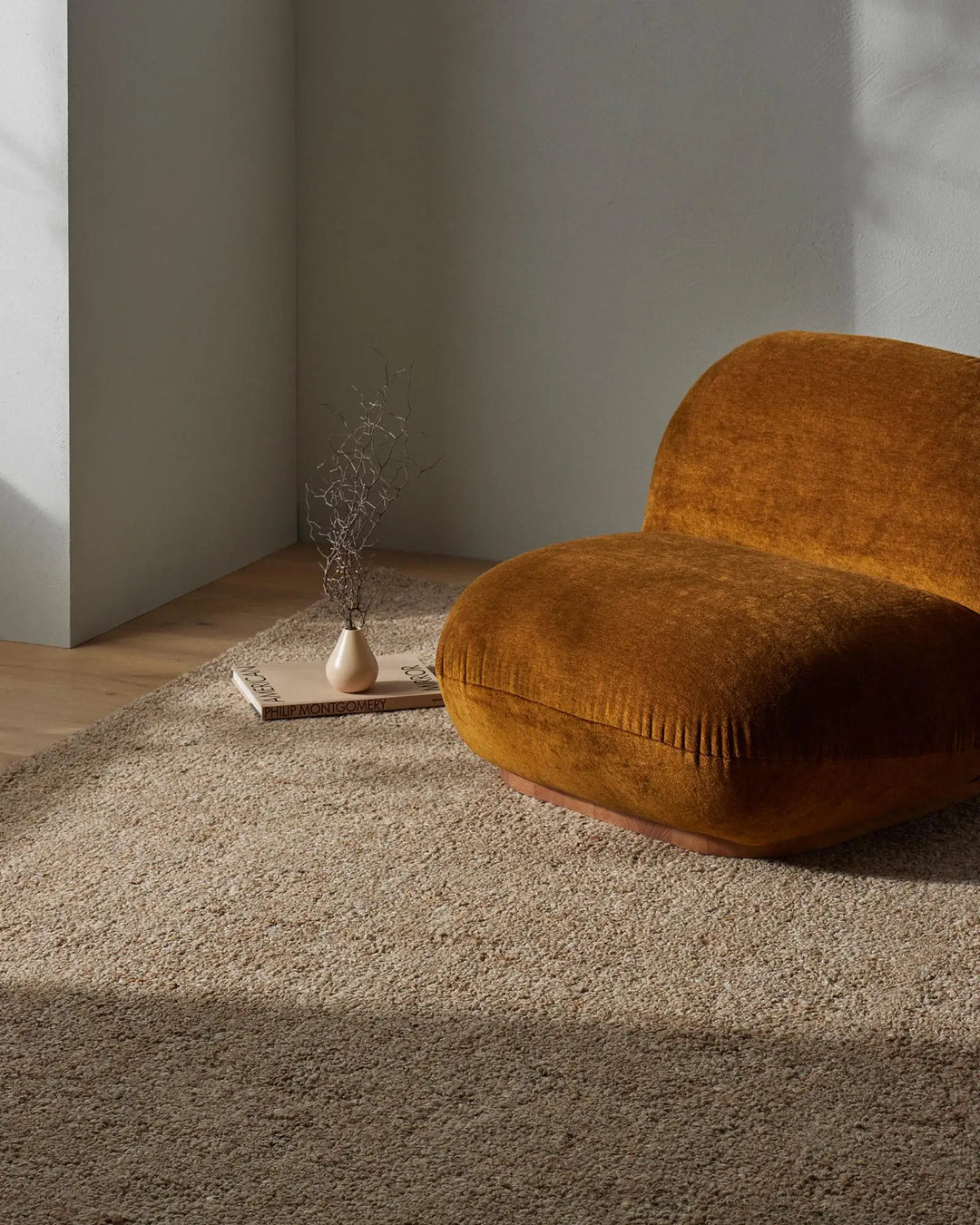 Warm ochre chair on taupe wool blend rug in minimalist room with soft natural light, beige walls, and sparse styling