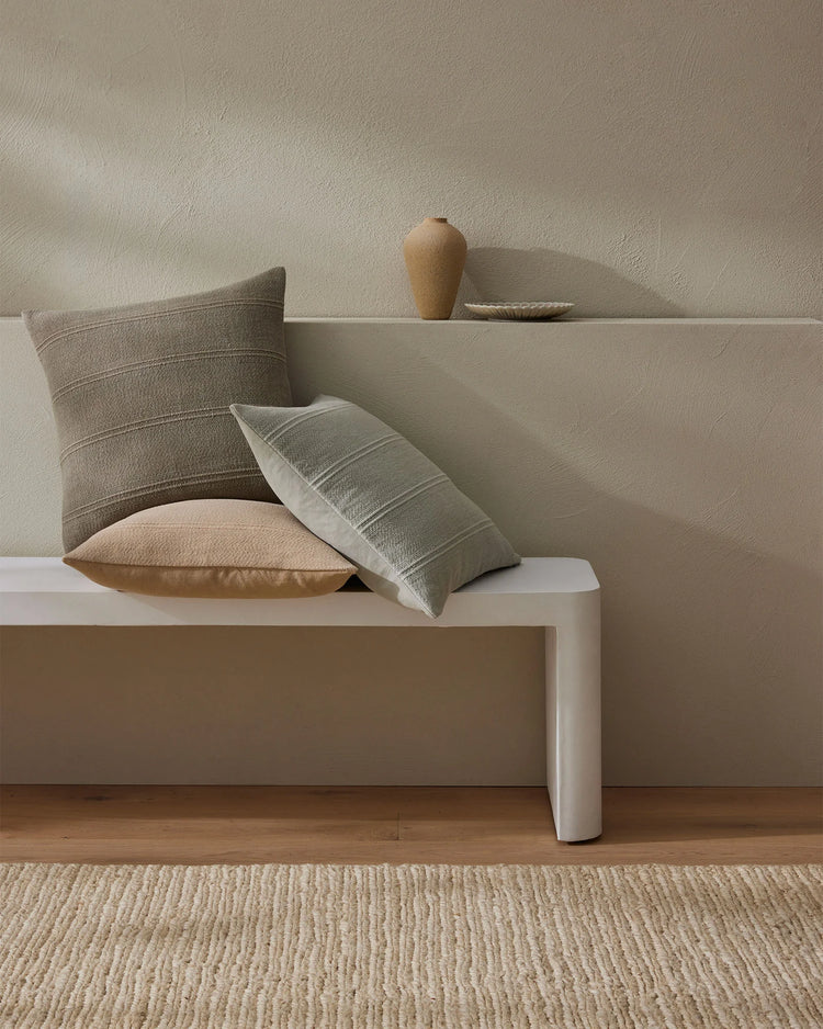 Minimalist living room styled with Palma cushions in neutral tones, featuring striped linen textures, warm wood flooring, and organic ceramic vessels on a platform bench