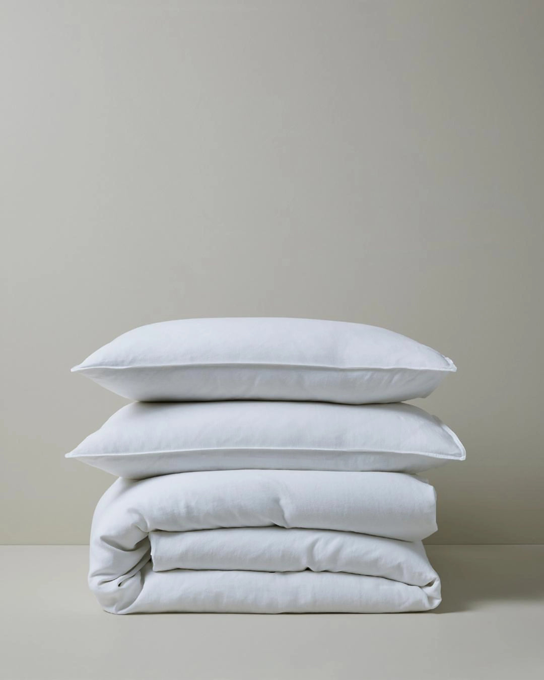 Stacked white linen bedding in minimalist aesthetic, featuring Ravello quilt cover and pillowcases with soft natural texture against neutral backdrop