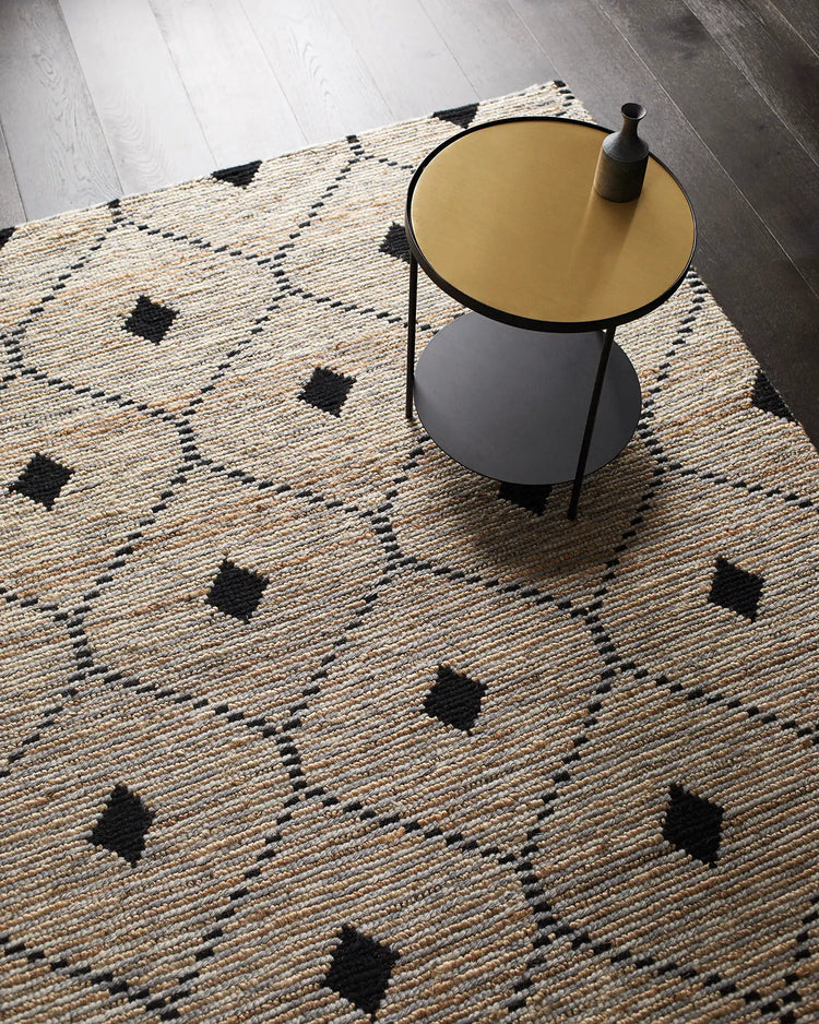 Natural jute rug with geometric black diamond pattern styled with mustard and charcoal side table on light wood floor