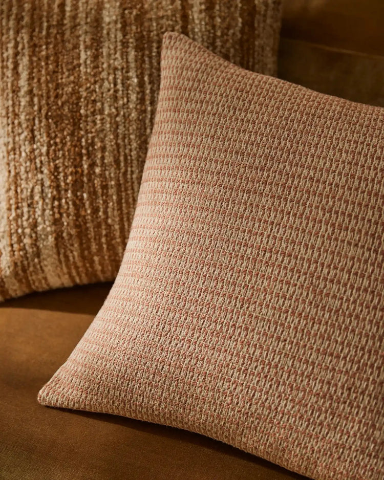 Neutral cushions in textured linen and wool blends layered on warm caramel upholstery, showcasing earthy minimalist home décor styling