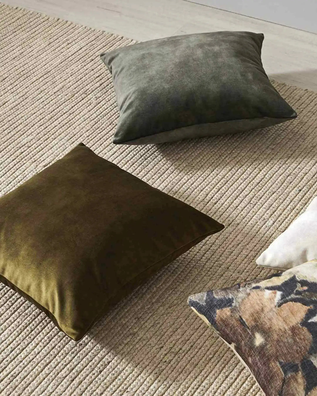 Earthy toned cushions in sage and olive arranged on a neutral ribbed rug, styled with textured home décor for a calm, minimalist interior aesthetic