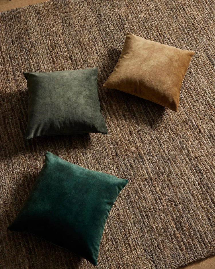 Three Ava cushions in jewel tones—emerald, jade and chartreuse—arranged on textured neutral wool rug for earthy, modern living room styling