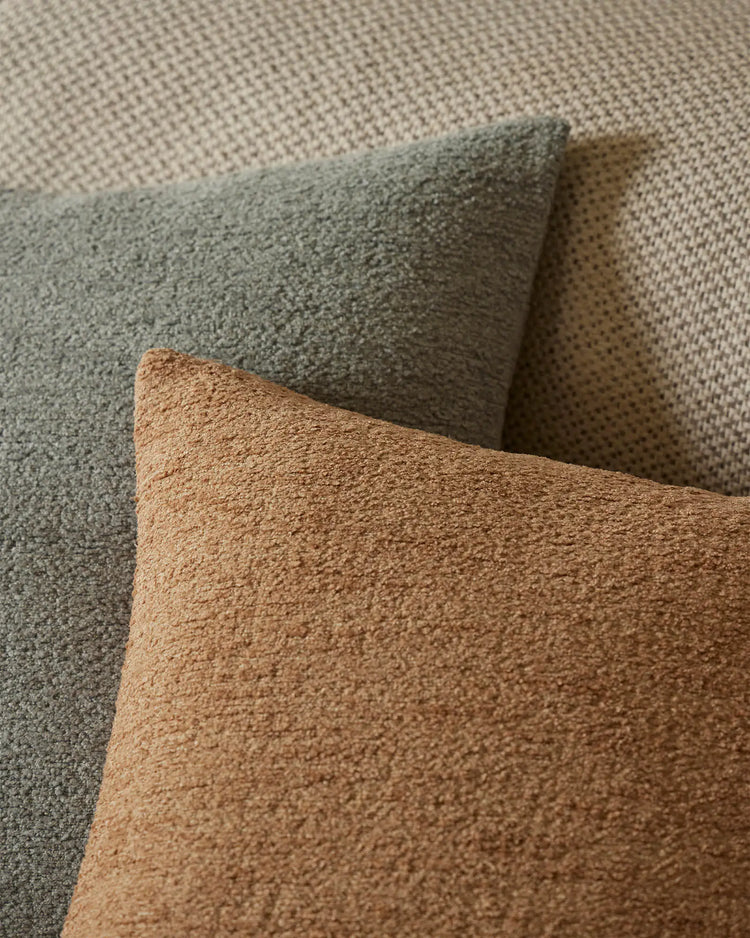 Earthy neutral cushion styling in sage and biscotti tones, layered textures of woven fabrics in muted earth palette, minimalist home décor aesthetic