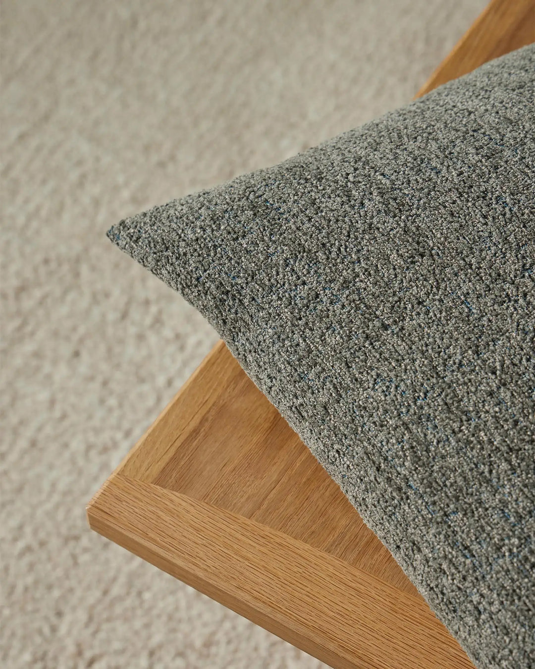 Sage green cushion with textured boucle weave on natural wood chair against neutral wall, showcasing minimalist Scandinavian aesthetic and soft layered palette