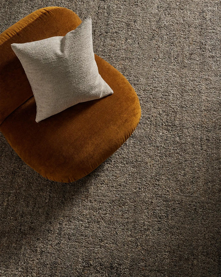 Warm mustard chair with cream cushion on textured grey wool blend rug, earthy neutral palette with tactile material contrast for contemporary home styling.