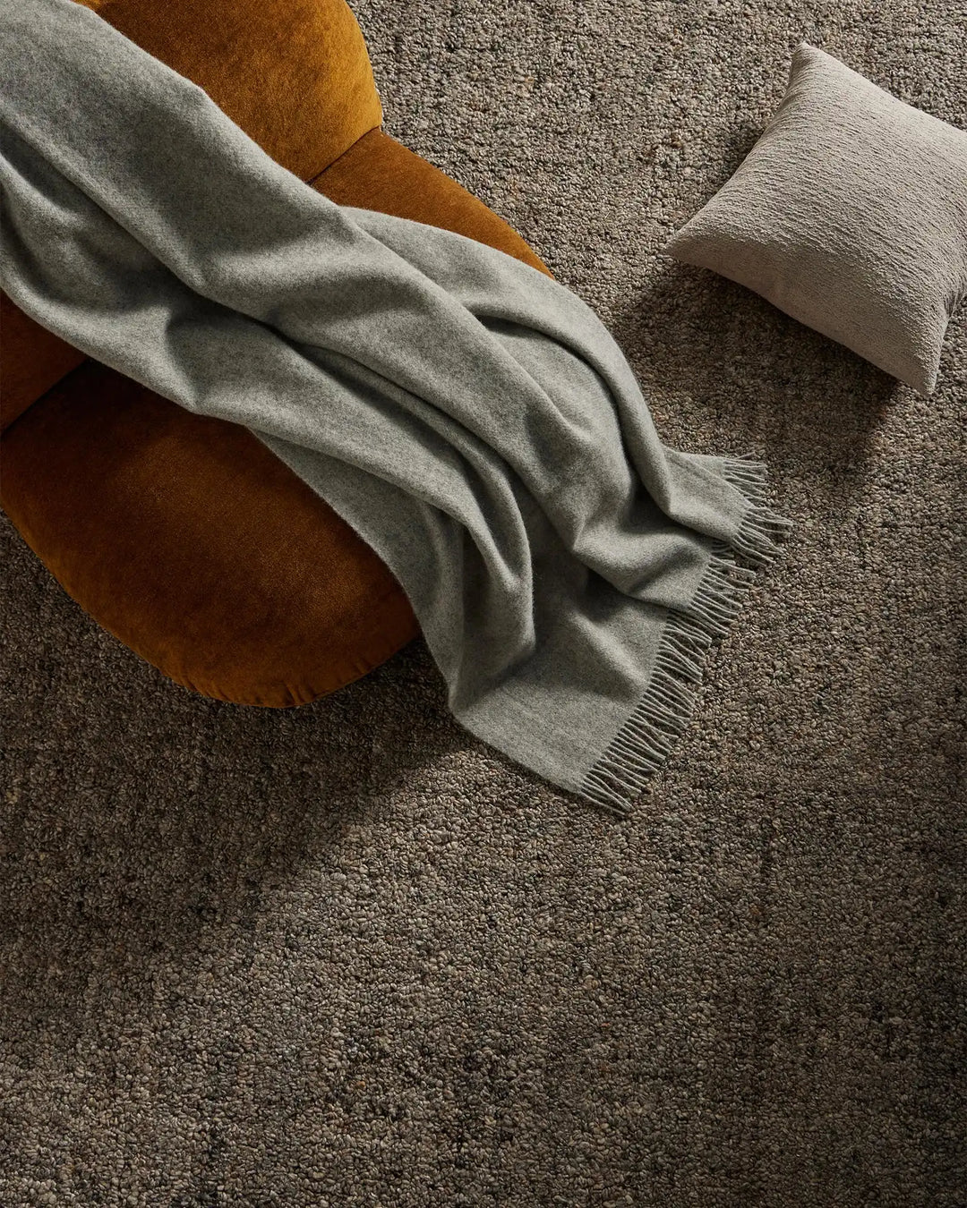 Warm mustard chair with sage throw and textured cushion arranged on charcoal wool-blend rug, earthy neutral styling for cosy living spaces