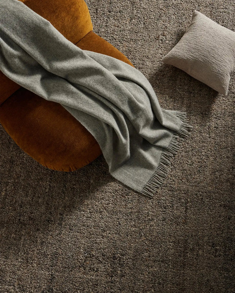 Warm mustard chair with sage throw and textured cushion arranged on charcoal wool-blend rug, earthy neutral styling for cosy living spaces