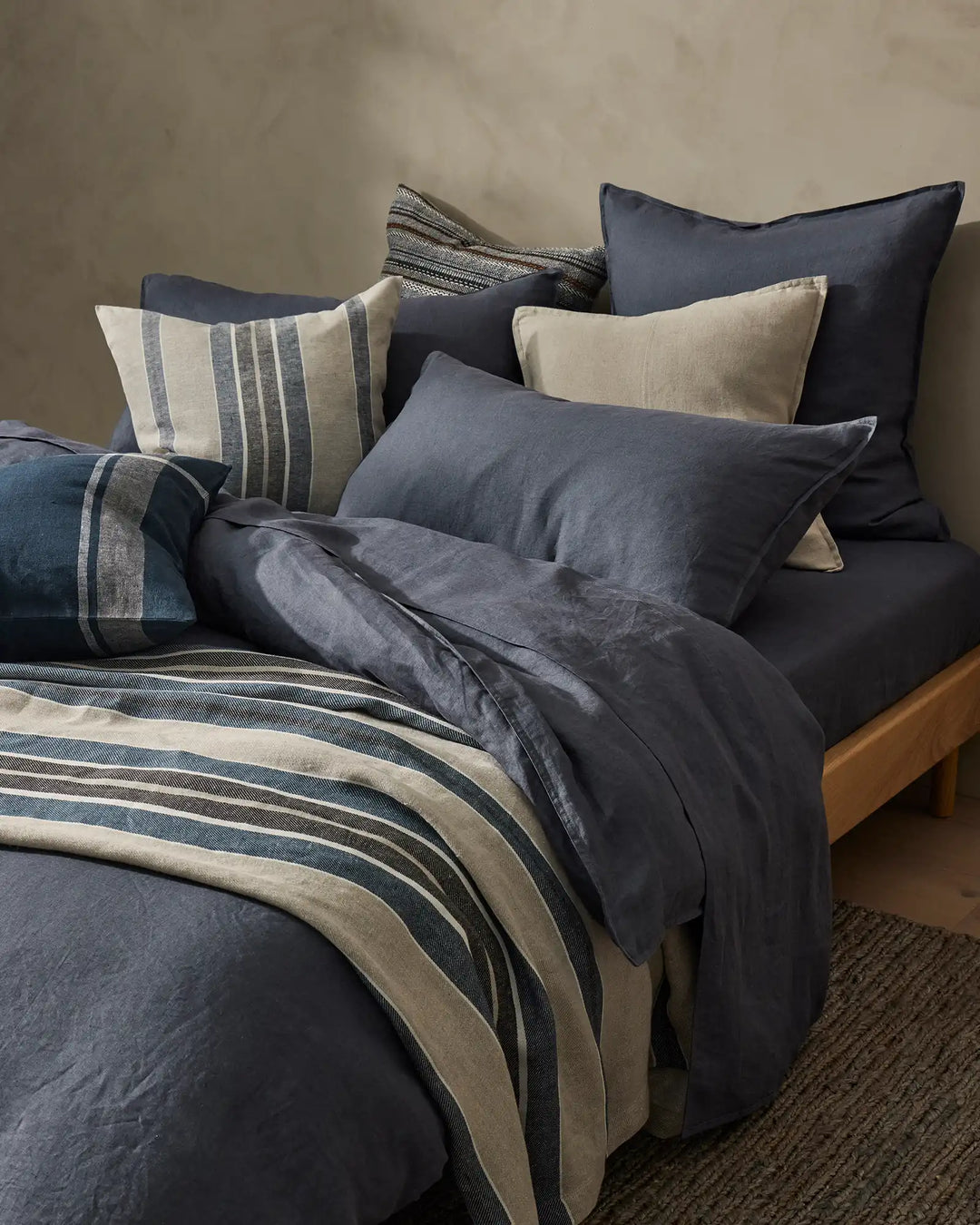 Layered bedding in indigo and natural linen tones with striped pillows, Ravello Quilt Cover and Franco cushions creating a serene, textured bedroom setting